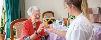 eine junge Pflegerin überreicht einer Bewohnerin Medikamante